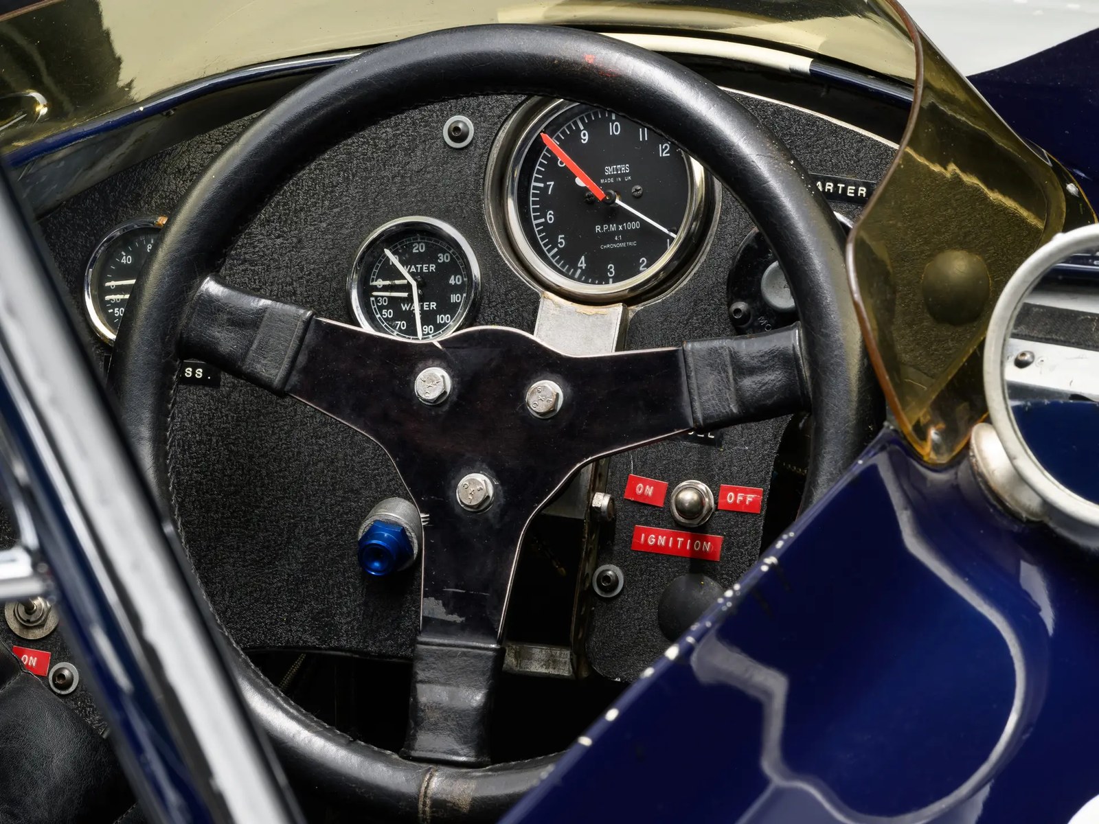 Inside 103. A Smiths chronometric tachometer reading to 12,000 rpm, a water-temperature gauge beside it, and an ignition toggle marked ON and OFF in red. The V-12 made its rated power at 10,500 rpm.
