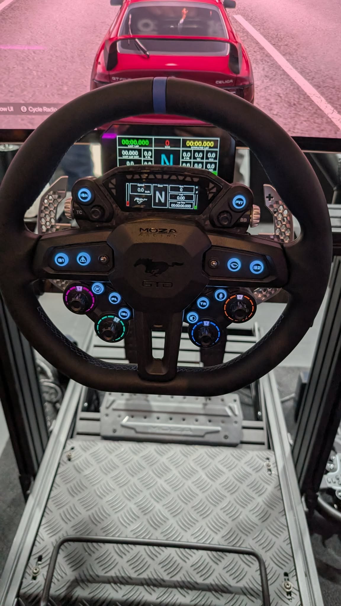 The Ford Mustang GTD wheel, running live on a simulator rig at the MOZA booth — round, heavily buttoned, with rear paddle shifters.
