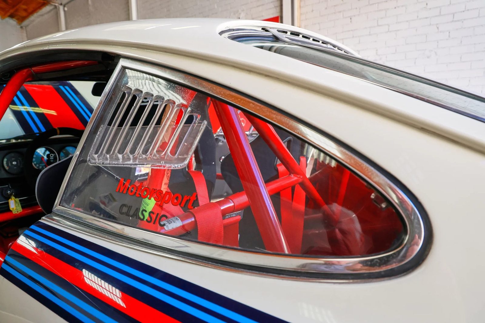 The welded 6-point roll cage and Sparco bucket seat, viewed through the rear quarter window — part of the early-1990s conversion from street car to dedicated vintage racer.